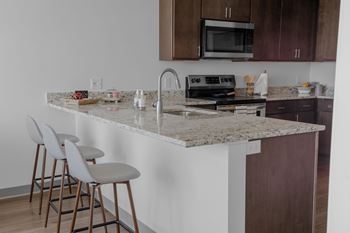 A kitchen with a granite countertop and white bar stools.